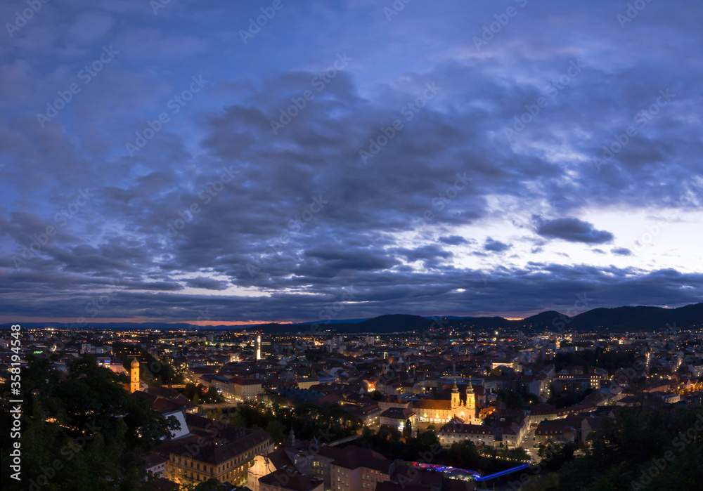 City lights of Graz and Mariahilfer church (Mariahilferkirche), view from the Shlossberg hill, in Graz, Styria region, Austria, after sunset. Panoramic view.
