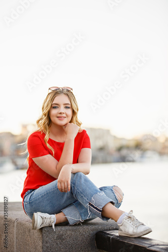 Beautiful girl walk in the summer Kiev City. Young woman tourist on a street. Street style portrait. Stylish girl near a river weared in red casual outfit. Life style. Local tourism. Srteet walk. 