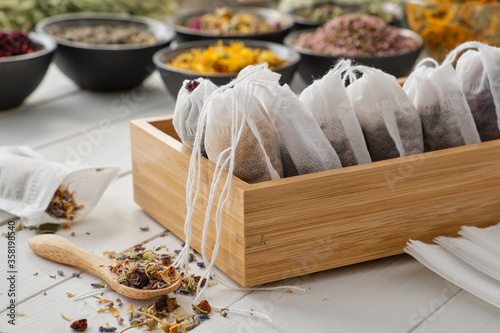 Wooden box of tea bags filled with dry medicinal herbs and flowers. Bowls of medicinal plants on background. Alternative medicine