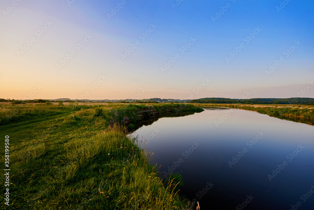 Beautiful blue Narew river flowing next to the green grass near Łomża