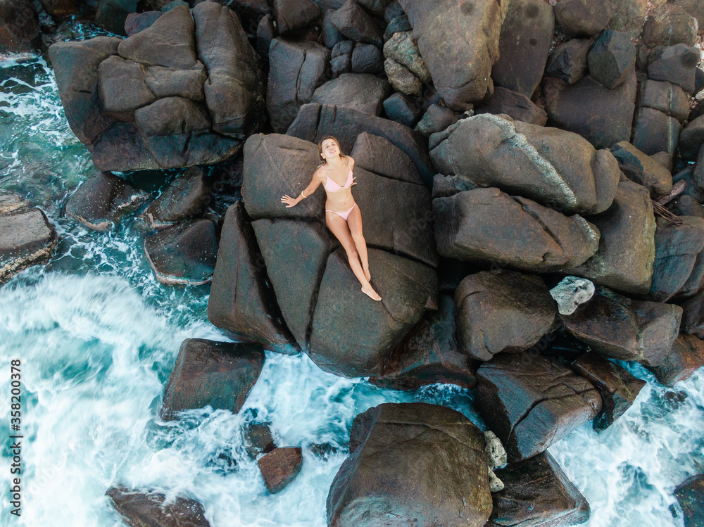 Beautiful slim blonde young woman in nude bikini sitting on rocks. Drone  aerial shot. Picturesque ocean landscape with girl from above. Summer  holiday in Sri Lanka Photos | Adobe Stock