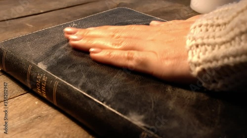 Woman cleaning dust off Holy Bible on table, closeup
