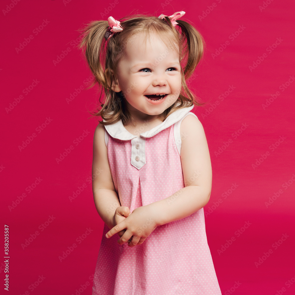 Emotion little girl with blue eyes in pink dress with two tail hairstyle, having fun and smiling. Pretty sweet kid happy playing at pink studio. Concept of kids fashion. Emotion little girl with blue eyes in pink dress with two tail hairstyle, having fun and smiling. Pretty sweet kid happy playing at pink studio. Concept of kids fashion.