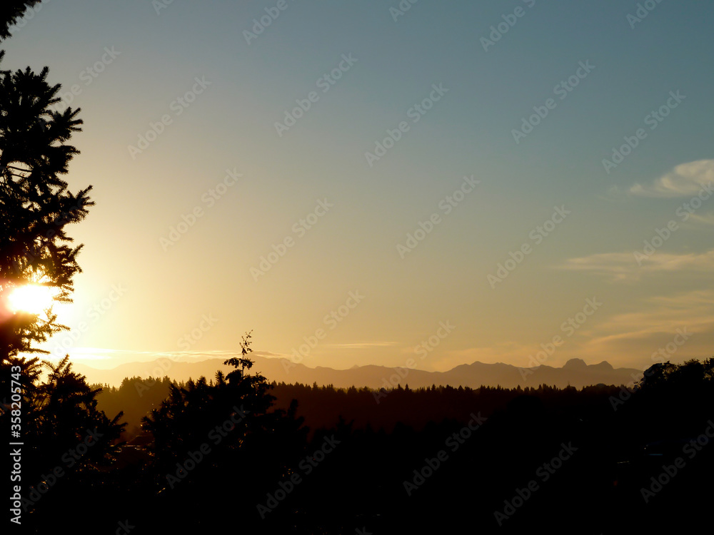 Obraz premium Bright sun and silhouette of the Northwest Cascades and evergreen forest of Washington State.