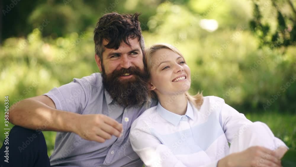 Loving couple hugging in the park. Summer spring couple. Happy girl and bearded guy spend time sitting in park on grass. Concept of relaxation in park. Loving couple hugging in the park. Summer spring couple. Happy girl and bearded guy spend time sitting in park on grass. Concept of relaxation in park.