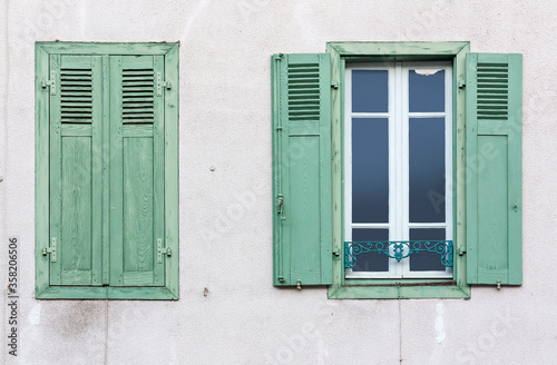 A window with open wooden shutters and window with closed shutters on a plastered wall