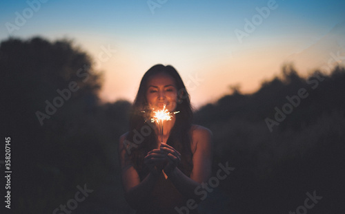 Abstract blur sparklers for celebration background,Motion by wind blurred woman hand holding burning Christmas sparkle on nature and twillight sky background.Winter vintage film grain filter style.