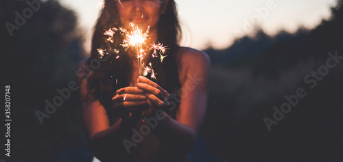 Abstract blur sparklers for celebration background,Motion by wind blurred woman hand holding burning Christmas sparkle on nature and twillight sky background.Winter vintage film grain filter style.