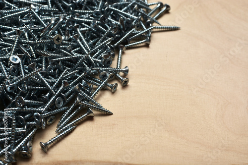 Metallic screws on a plywood sheet. Furniture manufacturing equipment, hardware and apartment repair tools. Industrial veneer background.