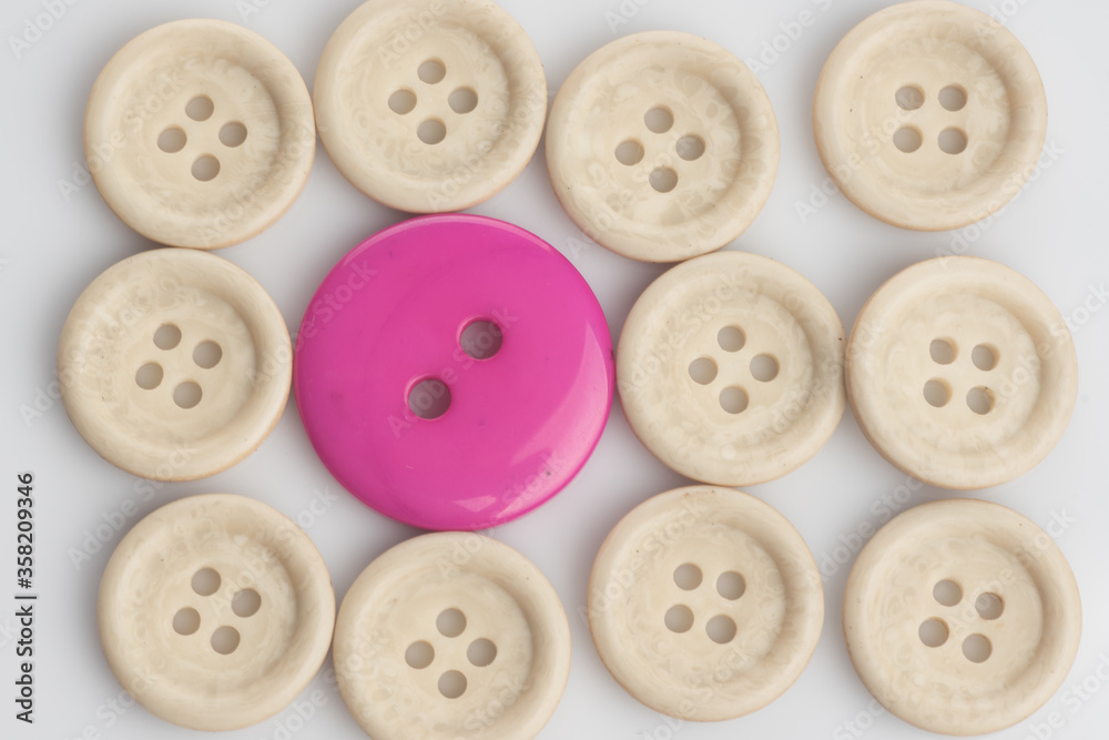 A single out pink button among white buttons,shot from top over a clear white surface A single out pink button among white buttons,shot from top over a clear white surface