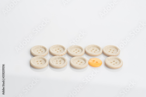 A single out yellow button among white buttons,shot from top over a clear white surface