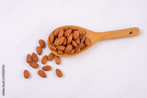 Almonds on wooden spoon isolated over white background. Top view