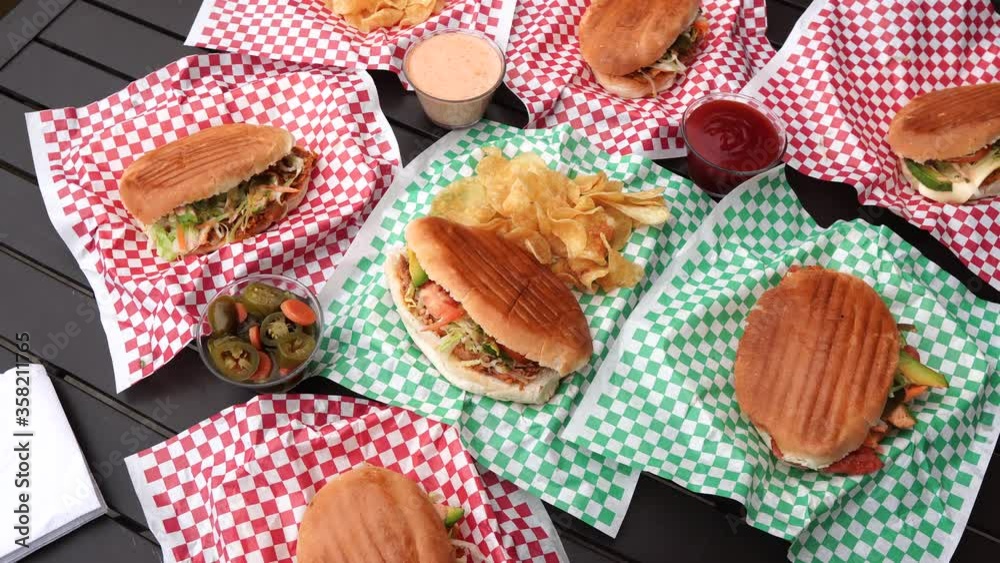 Overhead view of several delicious Mexican tortas with sauces and dressings, with a bowl of jalapeño pepper and a torta in the middle accompanied by potato chips