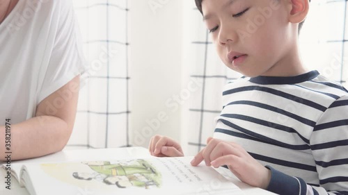 Cute little child is practicing and learning to read book by reading aloud with mother teaching phonics as daily routine at home. Reading and cognitive brain development and homeschool concept. photo