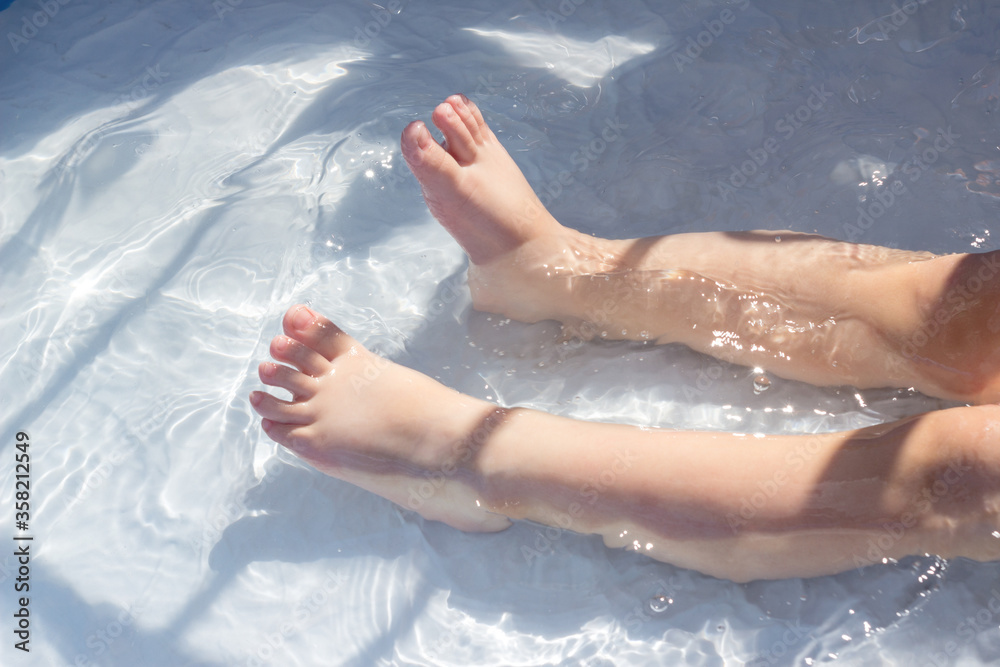 Feet of a child in the blue water of a children's pool. Fun summer outdoor activities, swimming and enjoying the water.