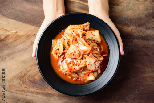 Kimchi cabbage on black plate holding by hand on wooden background  Korean food