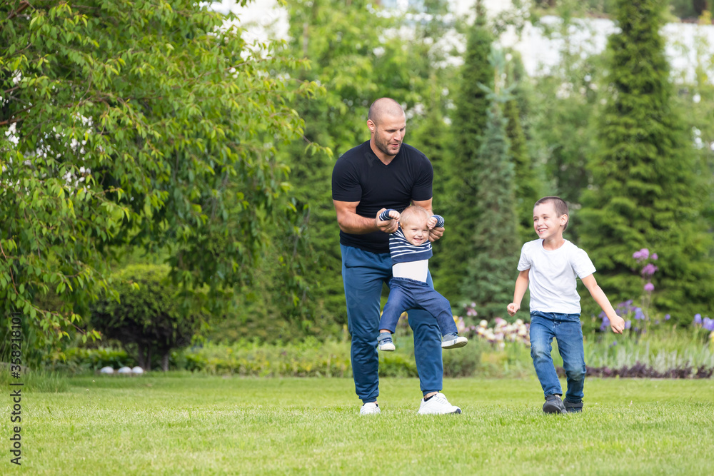 Cute cheerful two  boys brother child with  father  play outdoors in park. Happiness and harmony of family life. Great family vacation.