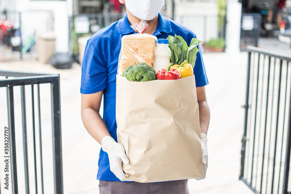 Deliver man wearing medical gloves and face mask in uniform handling bag and parcel box give to female costumer Postman and express grocery delivery service during covid19. Deliver man wearing medical gloves and face mask in uniform handling bag and parcel box give to female costumer Postman and express grocery delivery service during covid19.