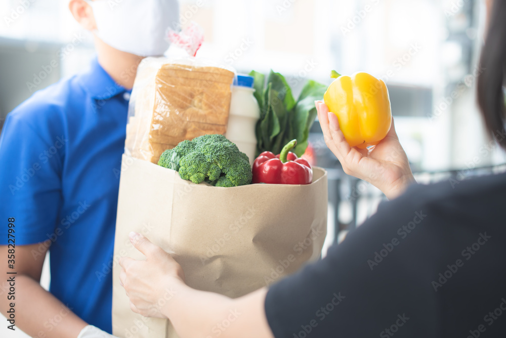 Deliver man wearing medical gloves and face mask in uniform handling bag and  parcel box give to female costumer Postman and express grocery delivery service during covid19.