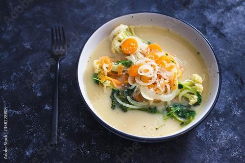 healthy plant-based food recipes concept, vegan soup with fresh veggies topping incuding caulini carrots onions and broccolini photo
