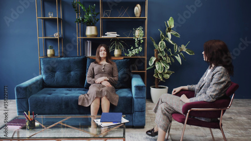 Young woman with closed eyes lying on sofa and listening psychologist at therapy session