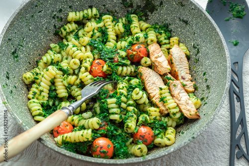 Pasta with spinach tomatoes and pieces of chicken fillet in a pan.