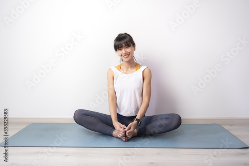 Portrait of young sporty Asian woman warm up exercise work out sitting on Yoga mat at home, healthy quarantine concept