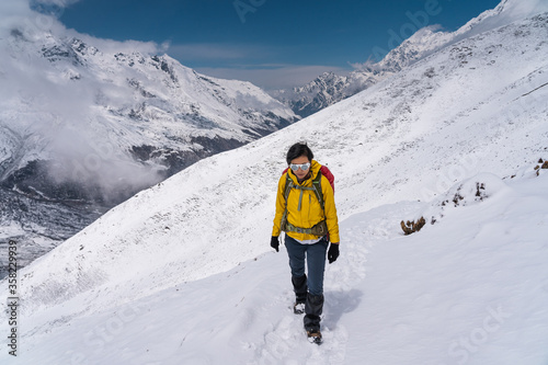 Young Asian woman trekking in Langtang valley after heavy snow storm. A woman trekking on trail that covered by fresh snow. Himalaya mountains range, Nepal