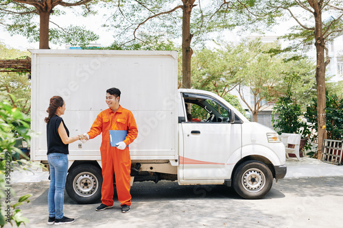 Asian moving man and mature woman standing against van shaking hands after making agreement, horizontal long shot, copy space