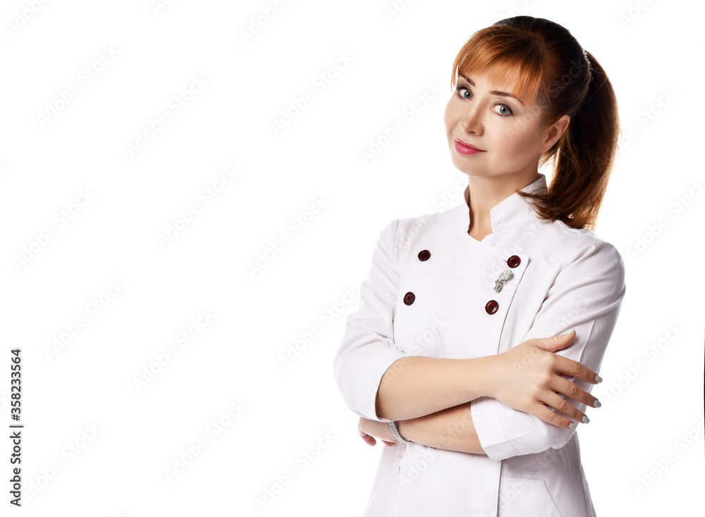 Young beautiful smiling red-haired woman doctor or nurse in white medical uniform standing with arms crossed over chest