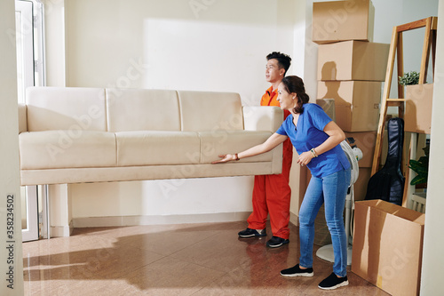 Mature Asian woman telling moving men where to put sofa they are carrying, horizontal shot, copy space © DragonImages