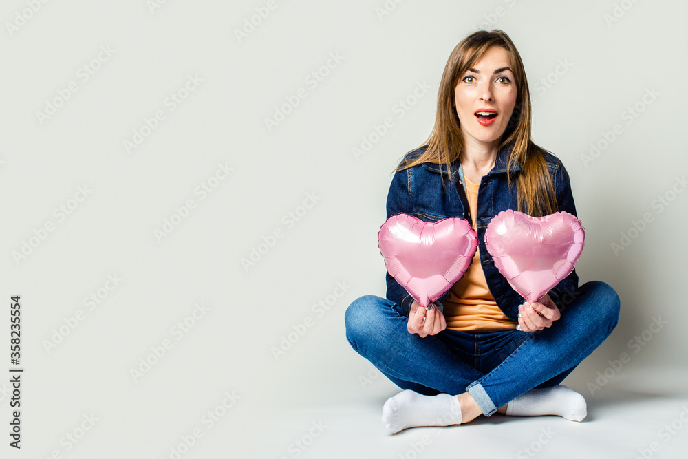 Surprised young woman sitting cross-legged holding a heart-shaped air balloons Surprised young woman sitting cross-legged holding a heart-shaped air balloons