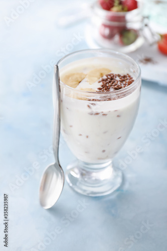 Glass of yogurt with banana and flax seeds on color background