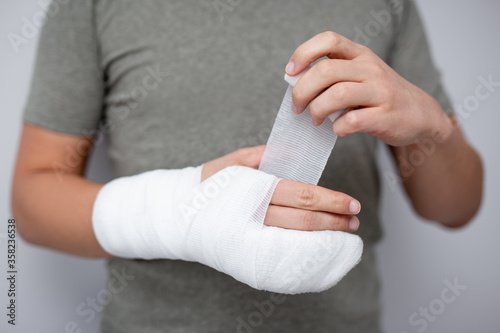 fracture and first aid concept - close up of man bandaging his hand after accident