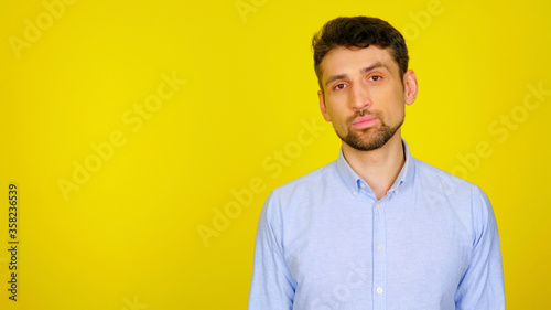 Handsome bearded man in a light blue shirt on a yellow background and with copyspace. Confident guy is looking at the camera