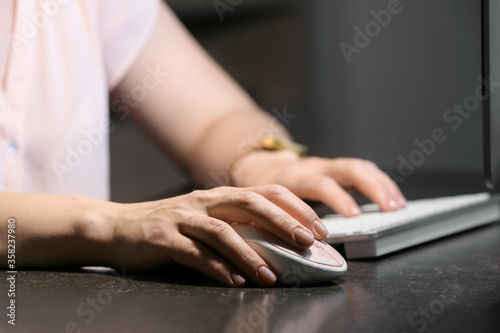 Woman using PC mouse while working on computer at table, closeup