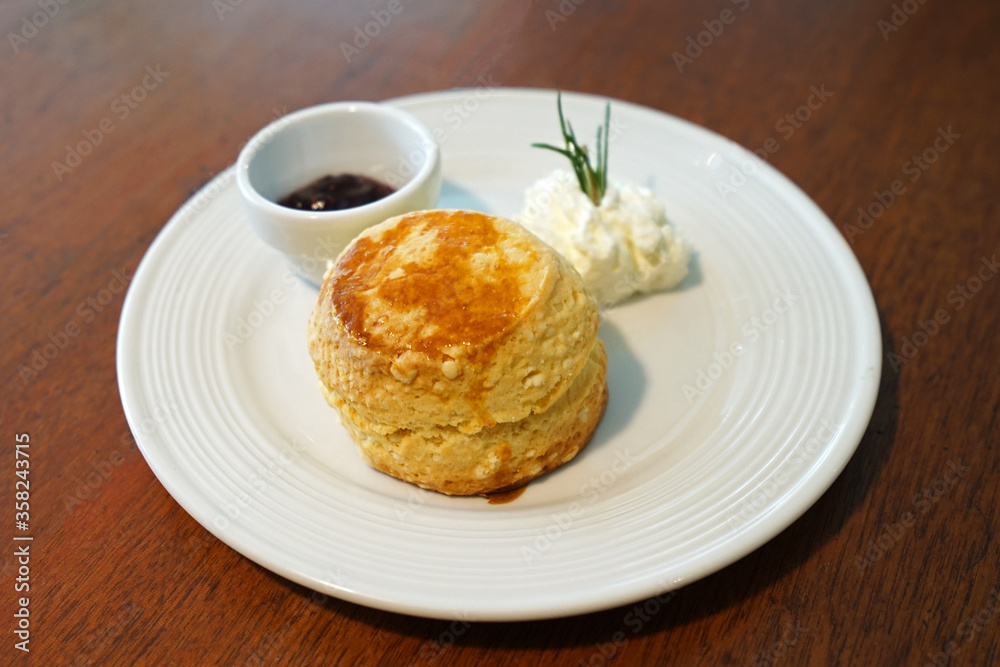 Close up butter scone with berries jam and clotted curd cream served on wooden table