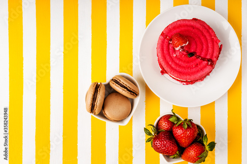 Chocolate macaroni cake, raspberry cake, fresh strawberries on a white and yellow striped background. photo