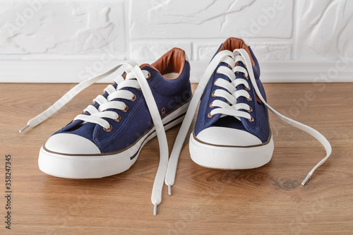 Pair of classic blue sneakers or gumshoes with white shoe laces on a floor. Comfortable shoes for fitness and sport.