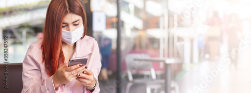 Asian woman wearing medical face mask for prevent dust and infection virus, using smartphone mobile phone in public, image banner size.