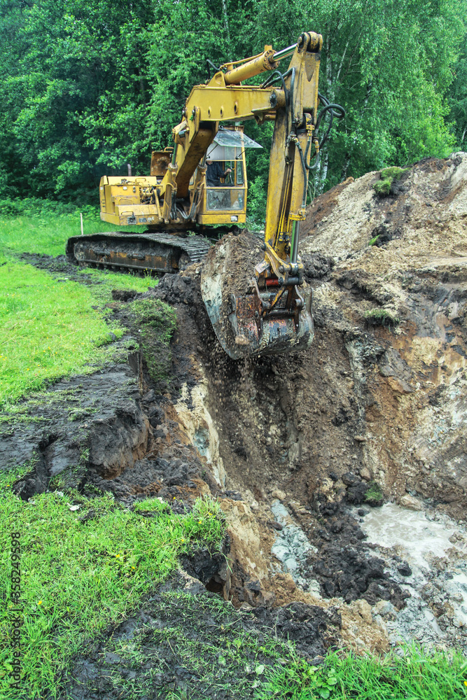 An excavator digs a large trench for building a house. A tractor digs a large lake that is already gaining water. Stock background for design An excavator digs a large trench for building a house. A tractor digs a large lake that is already gaining water. Stock background for design