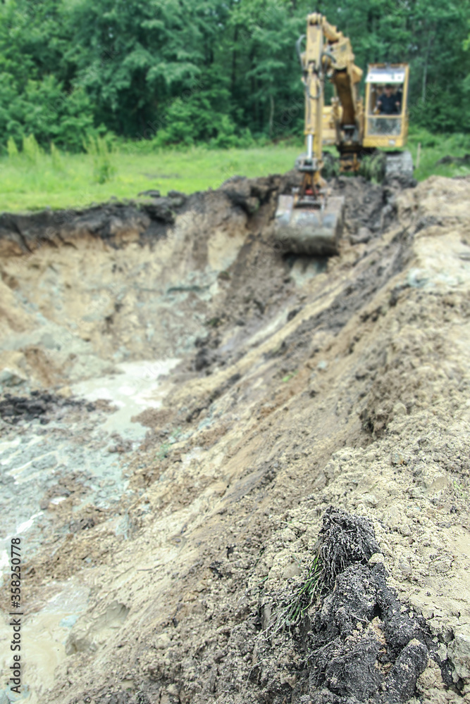 An excavator digs a large trench for building a house. A tractor digs a large lake that is already gaining water. Stock background for design An excavator digs a large trench for building a house. A tractor digs a large lake that is already gaining water. Stock background for design