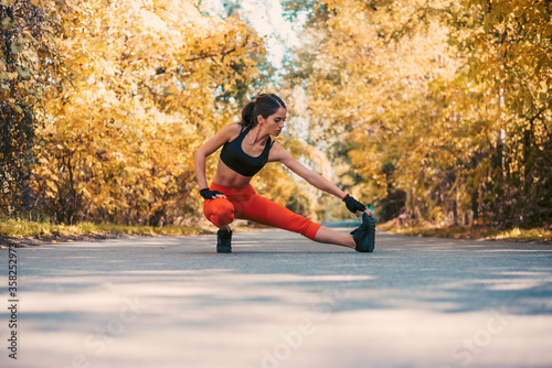 Young woman doing workout in the autumn park. Girl in sports bra doing stretching exercise.