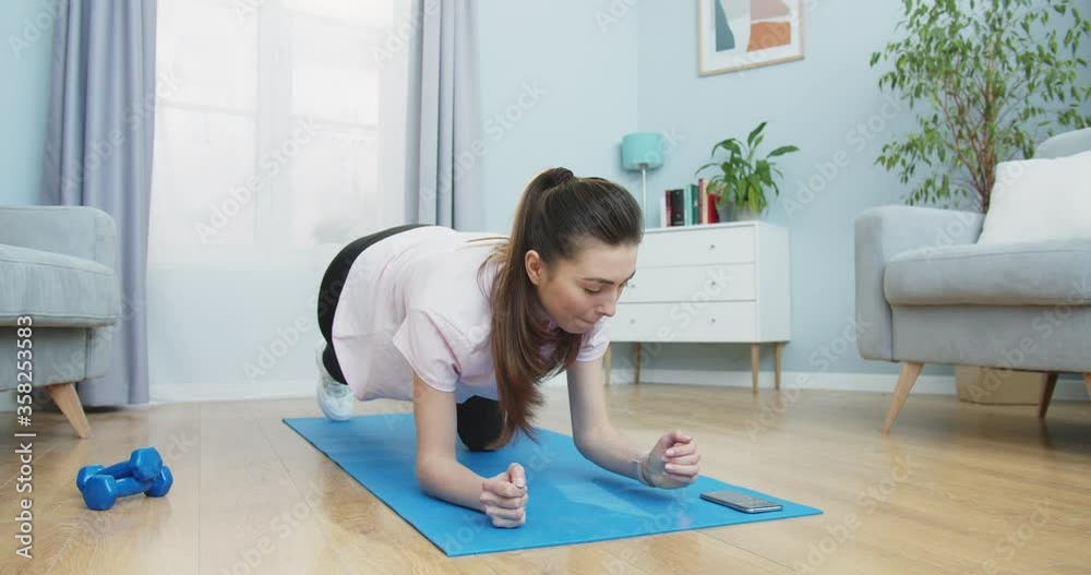 Middle side plan of fit girl switch on timer and start to do fitness workout at home. Brunette staying in the plank position. Healthy and sport lifestyle. Training, workout and wellness. Middle side plan of fit girl switch on timer and start to do fitness workout at home. Brunette staying in the plank position. Healthy and sport lifestyle. Training, workout and wellness.