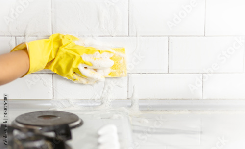 Hand and glove cleaning the kitchen tiles.