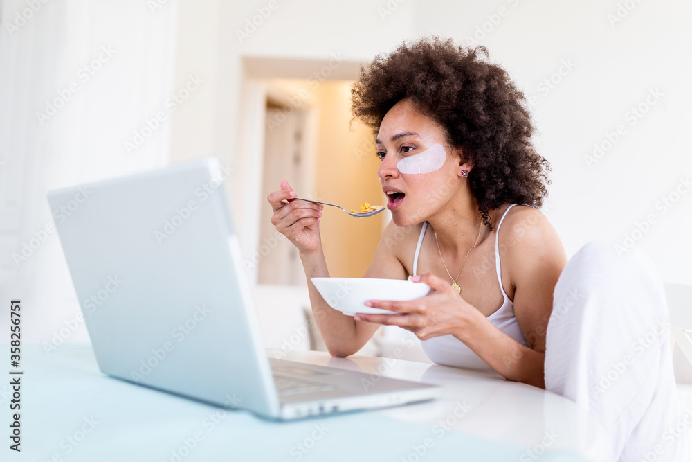 Attractive woman using her laptop computer while having breakfast and studying in home indoors. Freelance female model girl working on her laptop in the morning . Cup of milk with corn flakes Attractive woman using her laptop computer while having breakfast and studying in home indoors. Freelance female model girl working on her laptop in the morning . Cup of milk with corn flakes