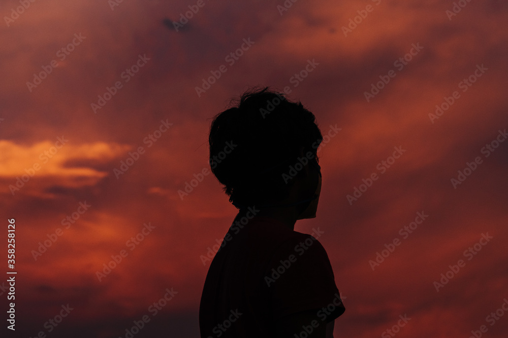 Silhouette of a kid in front of the beautiful dramatic sky during sunset
