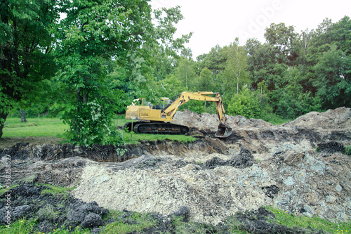 An excavator digs a large trench for building a house. A tractor digs a large lake that is already gaining water. Stock background for design