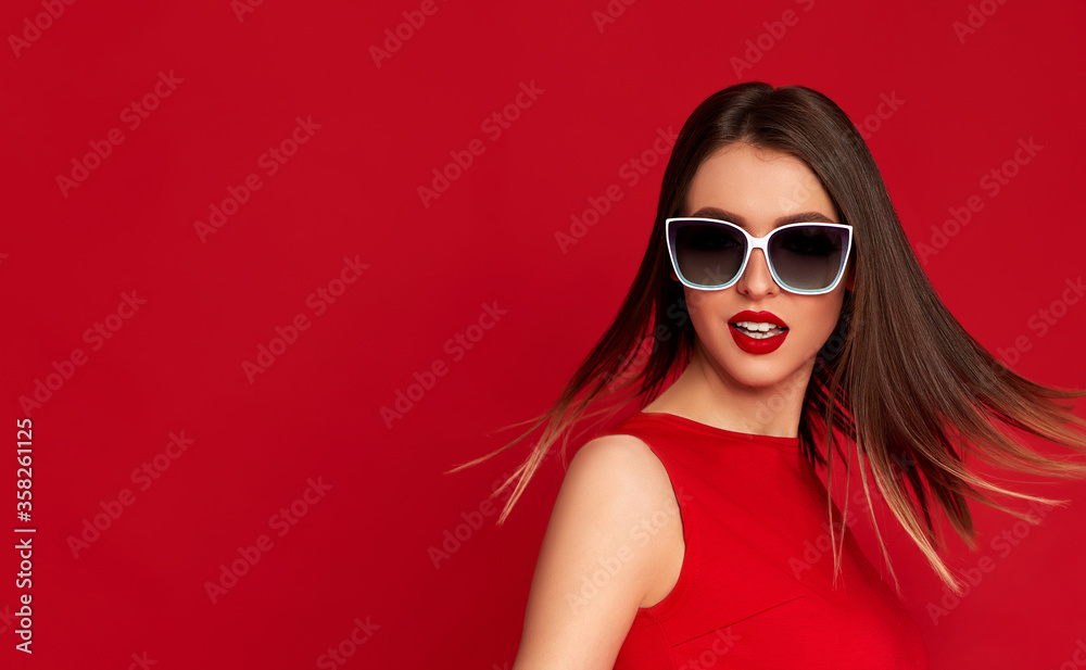 gorgeous brunette woman with flying hair and luxurious make-up in white sunglasses on red background. copy space