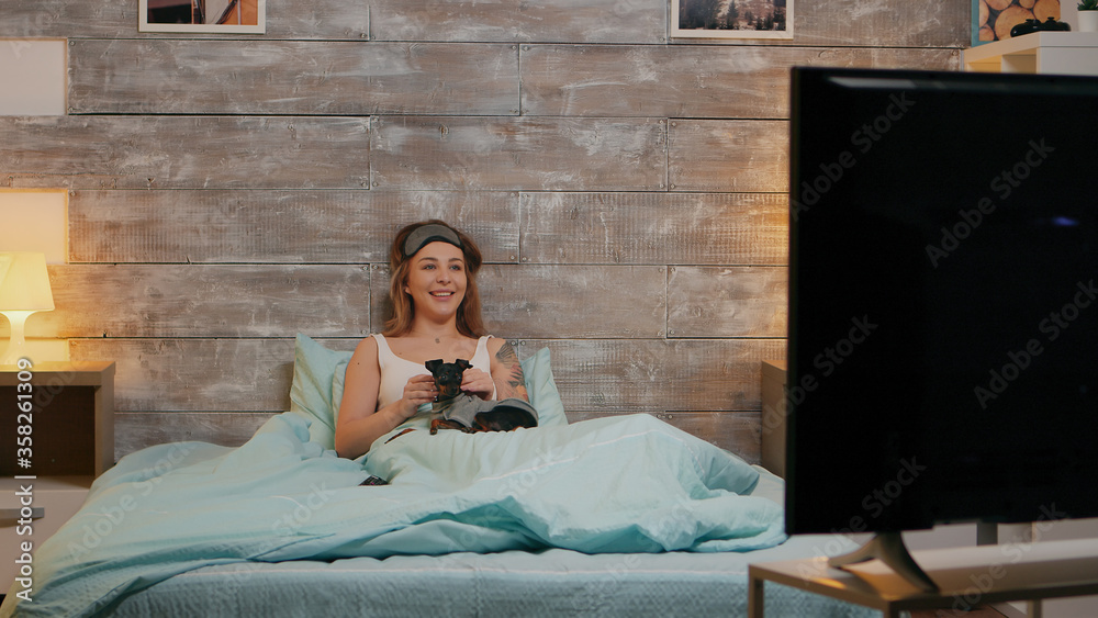 Obraz premium Zoom in shot of beautiful woman in pajamas at night watching tv with her dog.